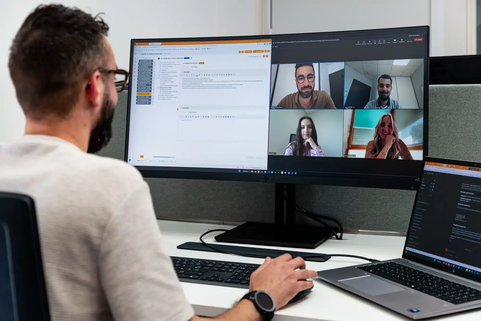 Écran d’ordinateur montrant une visioconférence avec quatre participants; à gauche, un homme avec lunettes et barbe travaille sur un logiciel affiché sur le grand moniteur et son ordinateur portable. Écran d’ordinateur montrant une visioconférence avec quatre participants; à gauche, un homme avec lunettes et barbe travaille sur un logiciel affiché sur le grand moniteur et son ordinateur portable.