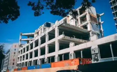 Hôtel à ossature béton en construction, passerelles ouvertes et conteneurs de chantier colorés au premier plan.