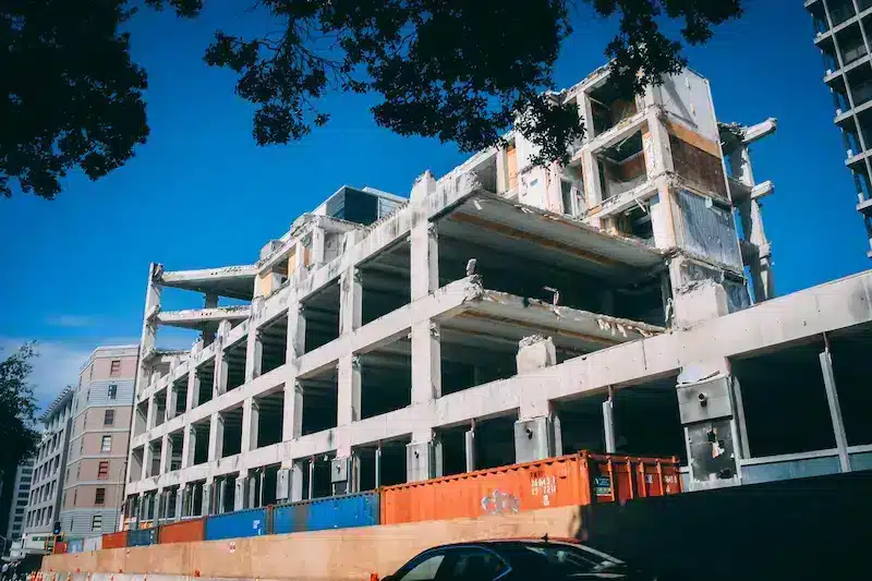 Hôtel à ossature béton en construction, passerelles ouvertes et conteneurs de chantier colorés au premier plan.
